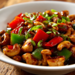 Close-up of authentic cashew chicken stir-fry with diced chicken, crunchy cashews, green bell peppers, and scallions coated in glossy soy and oyster sauce served in a white bowl on rustic wood.