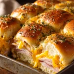 Close-up of baked turkey and cheese sliders with golden brown tops, melted cheddar cheese, and layers of sliced turkey inside soft slider buns, garnished with dried parsley on a wooden board