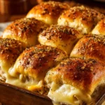 Close-up of baked turkey and cheese sliders in a rustic rectangular dish showing golden brown tops, melted Swiss cheese, sliced turkey breast, and poppy seed butter Dijon glaze on soft slider buns
