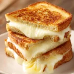 Close-up top-down view of a grilled mozzarella sandwich with crispy golden brown bread and melted mozzarella oozing on a white plate