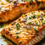 Close-up of air fryer salmon with lemon slices and garlic butter sauce on a white plate.