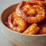Close-up of air fryer shrimp with a crispy texture, garnished with herbs on a clean white plate.