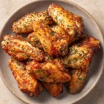 Crispy air fryer chicken wings with Italian seasoning on a plate with a light background.