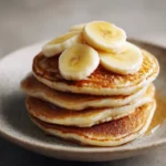 Close-up of fluffy banana pancakes stacked with syrup drizzling down.