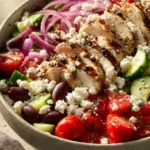 Close-up of a Greek chicken bowl with vibrant ingredients and fresh herbs.