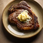 Close-up of a pan-seared steak with melting butter on top, showcasing a juicy and appetizing texture.