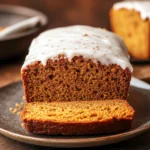 Close-up of pumpkin bread with icing on a wooden board, showcasing its texture and glaze.