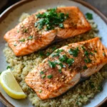 Close-up of air fryer salmon with quinoa on a white plate, garnished with herbs.