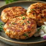 Close-up of golden-brown chicken breast patties on a white plate with minimal background.