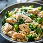 Close-up of a creamy one pot chicken orzo with broccoli, garnished with herbs.