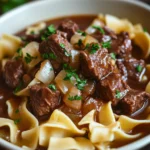 Close-up of slow cooker beef and noodles with a rich sauce and garnished with herbs.