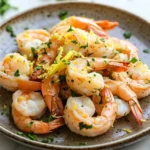 Air fryer shrimp lemon - the image shows a plate of cooked shrimp on a white marble countertop. the shrimp are arranged in a circular pattern on the plate, with some overlapping each other. they are orange in color and appear to be seasoned with herbs and spices. the plate is garnished with chopped parsley, adding a pop of green color to the dish. the background is blurred, but it appears to be a kitchen countertop with more parsley scattered around.