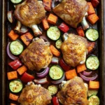 Baked chicken and vegetables sheet pan - the image shows a rectangular baking tray filled with roasted chicken and vegetables. the chicken is golden brown and appears to be seasoned with herbs and spices. the vegetables are cut into small cubes and are arranged in a circular pattern around the chicken. there are also sliced zucchini, carrots, and red onions scattered throughout the tray. the tray is placed on a wooden table.