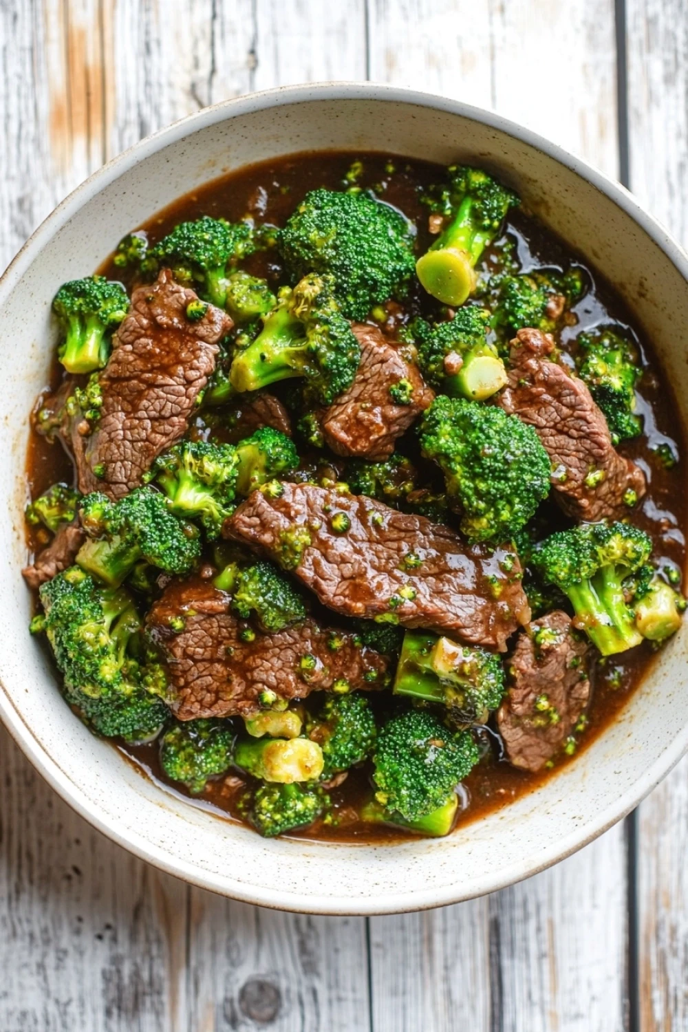 Beef and broccoli freezer meal crock pot - the image is a close-up of a bowl of beef and broccoli stir-fry. the beef is cooked medium-rare and appears to be seasoned with herbs and spices. the broccoli is bright green and looks fresh and healthy. the dish is served in a white ceramic bowl with a brown rim. the background is a wooden table with a rustic texture. the overall color palette of the image is warm and inviting.