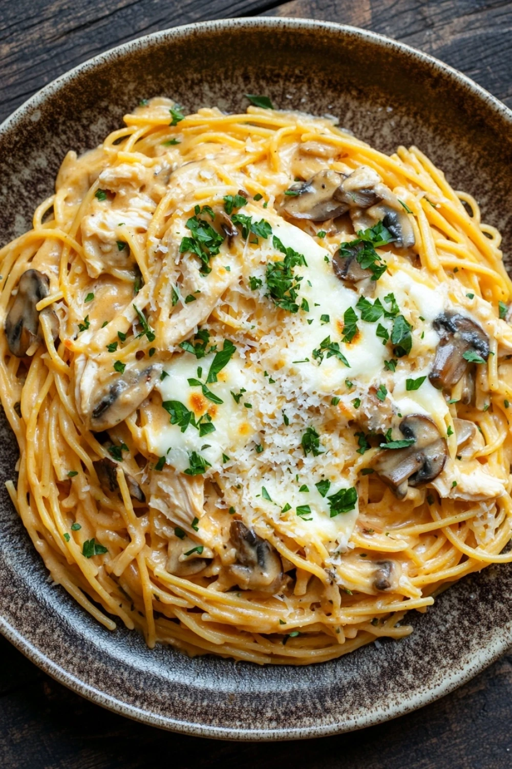 Freezer chicken tetrazzini - the image is a close-up of a plate of spaghetti dish. the spaghetti is cooked al dente and is covered in a creamy sauce with chunks of chicken and mushrooms. the sauce is drizzled over the top with a sprinkle of parmesan cheese. the dish is garnished with fresh parsley. the plate is sitting on a wooden table with a dark background.