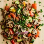 Ground beef dinner gf - the image is a close-up of a colorful salad on a wooden cutting board. the salad is made up of various vegetables, including zucchini, bell peppers, and mushrooms. the vegetables are arranged in a circular pattern, with some overlapping each other. the ground is a light brown color, and there are small pieces of minced meat scattered throughout the salad. there are also some chopped parsley scattered throughout, adding a pop of green color to the dish. the overall appearance of the salad is fresh and appetizing.