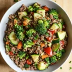 Ground beef dinner macro friendly - the image is a close-up of a bowl of quinoa salad. the bowl is white and is placed on a wooden table. the quinoa is a light brown color and is mixed with various vegetables such as broccoli, zucchini, carrots, and bell peppers. the vegetables are bright green and appear to be seasoned with herbs and spices. there are also a few sprigs of parsley scattered around the bowl. the overall appearance of the salad is colorful and appetizing.