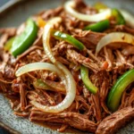 Italian beef slow cooker - the image is a close-up of a plate of food. the plate is round and has a speckled pattern. the food appears to be a dish made with shredded beef, sliced onions, and green bell peppers. the beef is cooked to a medium-rare and the onions are sliced into thin strips. the bell peppers are bright green and appear to be seasoned with spices. the dish is garnished with a sprinkle of herbs and spices, adding a pop of color to the plate. the background is dark, making the plate and its contents stand out.