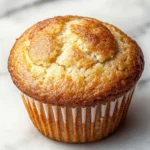 Martha white muffin mix with greek yogurt - the image is of a freshly baked muffin on a white marble surface. the muffin is golden brown in color and has a crumbly texture on top. it appears to be soft and fluffy, with a light dusting of powdered sugar on top, giving it a golden-brown color. the edges of the muffin are slightly curled, indicating that it has been freshly baked. the background is blurred, making the muffins the focal point of the image.