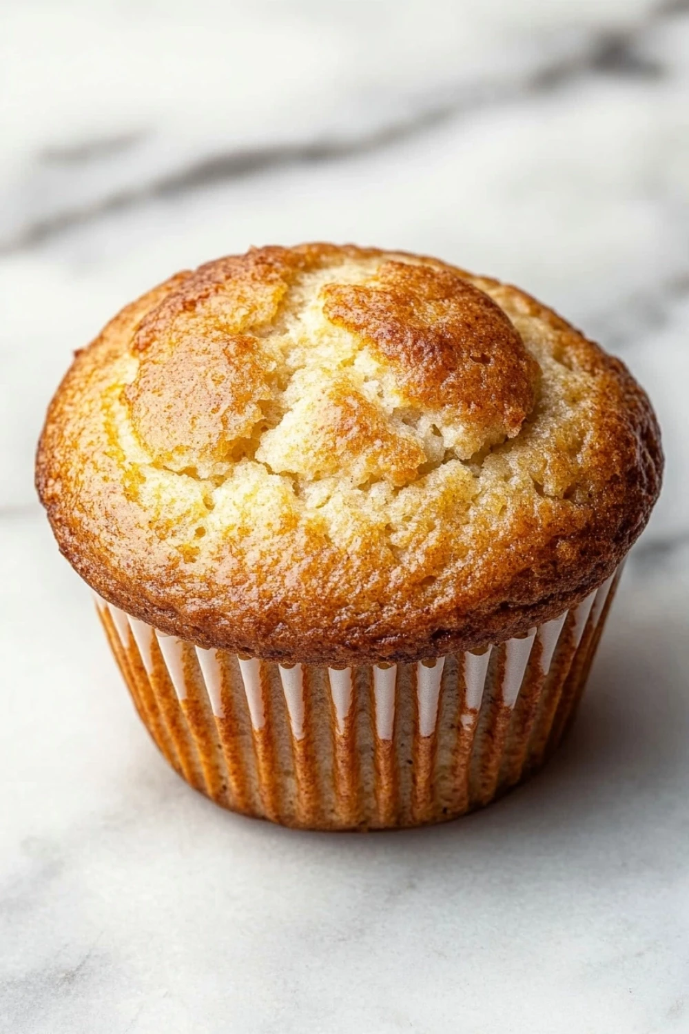 Martha white muffin mix with greek yogurt - the image is of a freshly baked muffin on a white marble surface. the muffin is golden brown in color and has a crumbly texture on top. it appears to be soft and fluffy, with a light dusting of powdered sugar on top, giving it a golden-brown color. the edges of the muffin are slightly curled, indicating that it has been freshly baked. the background is blurred, making the muffins the focal point of the image.