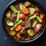 One pot beef and veggies - the image is a close-up of a bowl of beef stew. the stew is made with chunks of beef, carrots, potatoes, and celery. the beef is cooked in a rich, dark brown broth and is garnished with chopped herbs. the vegetables are cut into small cubes and are arranged in a circular pattern around the beef. the bowl is black and is sitting on a dark, textured surface. there are a few sprigs of parsley scattered around the bowl.
