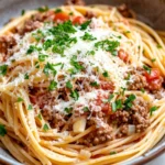 One pot beef garlic pasta - the image is a close-up of a plate of spaghetti bolognese. the spaghetti is cooked al dente and is topped with a generous amount of ground beef, tomato sauce, and grated parmesan cheese. the dish is garnished with fresh parsley. the plate is made of ceramic and is sitting on a white countertop. the background is blurred, making the spaghetti the focal point of the image.