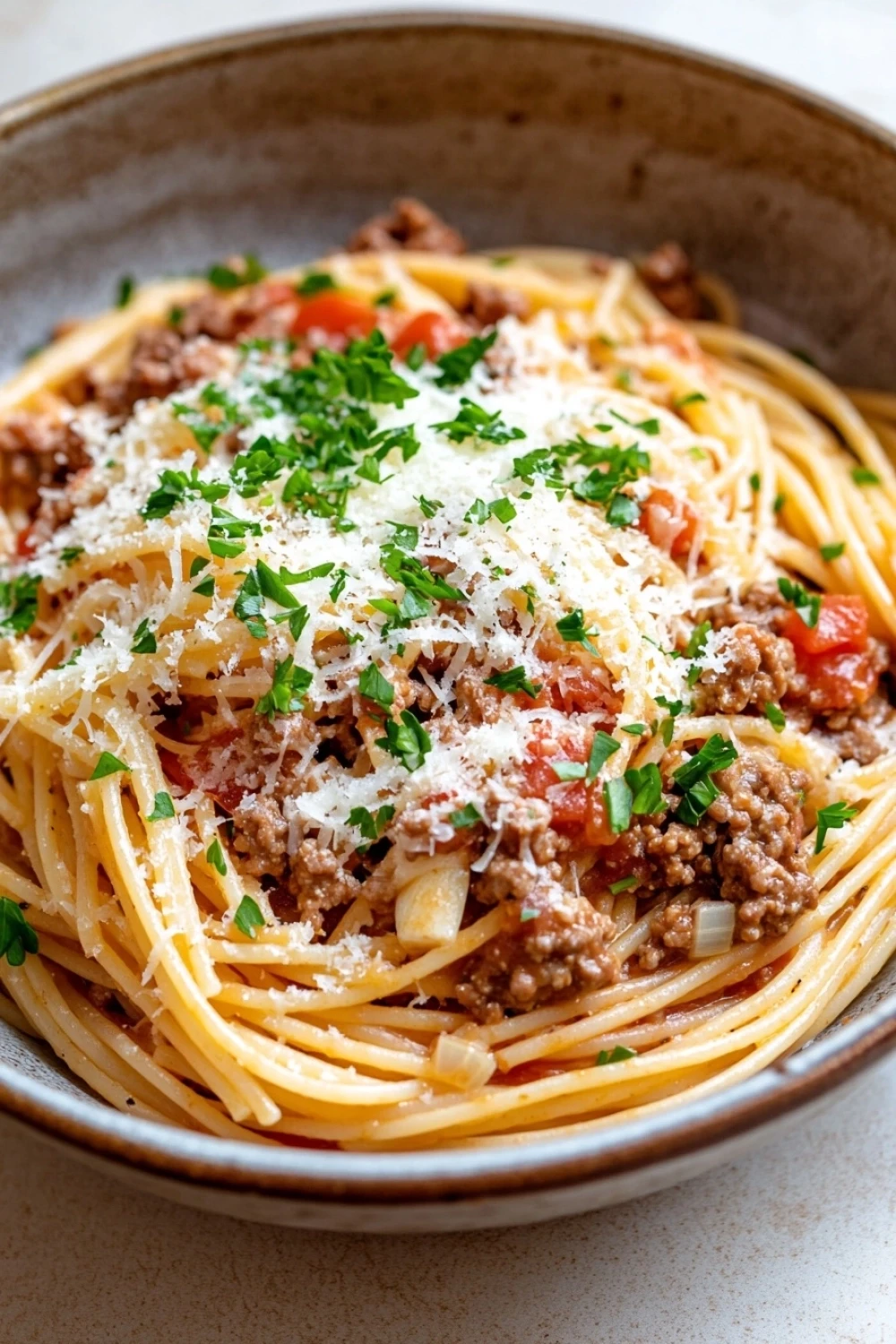 One pot beef garlic pasta - the image is a close-up of a plate of spaghetti bolognese. the spaghetti is cooked al dente and is topped with a generous amount of ground beef, tomato sauce, and grated parmesan cheese. the dish is garnished with fresh parsley. the plate is made of ceramic and is sitting on a white countertop. the background is blurred, making the spaghetti the focal point of the image.