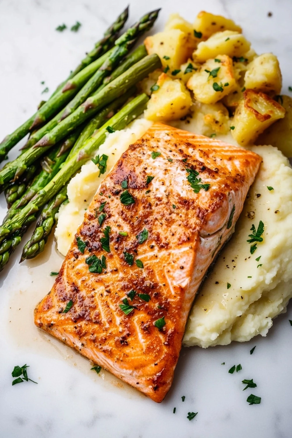 Salmon dinner aesthetic - the image shows a plate of food consisting of a piece of salmon, mashed potatoes, and asparagus. the salmon is cooked to a golden brown color and is garnished with fresh herbs. the mashed potatoes are white and fluffy, and the aspartagus is a bright green color. the plate is white and the food is arranged neatly on a marble surface. the overall presentation of the dish is elegant and appetizing.