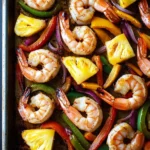 Sheet pan shrimp fajitas with pineapple - the image shows a baking tray filled with shrimp and vegetables. the shrimp are cooked medium-sized and have a pinkish-orange color. they are arranged in a circular pattern on the tray, with some overlapping each other. the vegetables include red, yellow, green, and orange bell peppers, as well as sliced pineapples and red onions. the tray is lined with parchment paper, and the background is dark. the overall appearance of the dish is colorful and appetizing.