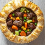 Slow cooker beef pot pie - the image is a close-up of a beef pot pie. the pie is golden brown and has a flaky crust. it is filled with chunks of beef, carrots, peas, and corn. the beef is cooked to a medium-rare and appears to be seasoned with herbs and spices. the vegetables are arranged in a circular pattern around the edges of the pie, creating a colorful and appetizing dish. the background is a wooden surface, which contrasts with the warm tones of the food.