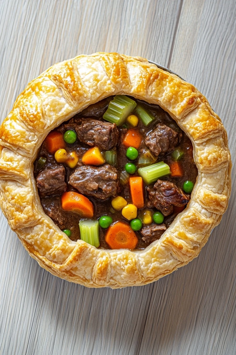Slow cooker beef pot pie - the image is a close-up of a beef pot pie. the pie is golden brown and has a flaky crust. it is filled with chunks of beef, carrots, peas, and corn. the beef is cooked to a medium-rare and appears to be seasoned with herbs and spices. the vegetables are arranged in a circular pattern around the edges of the pie, creating a colorful and appetizing dish. the background is a wooden surface, which contrasts with the warm tones of the food.