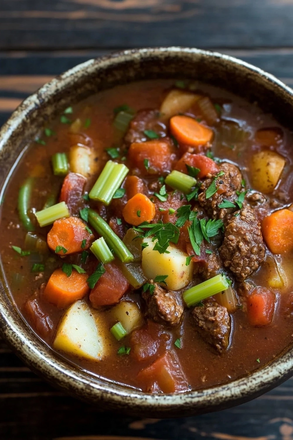 Slow cooker soup stew - the image is a close-up of a bowl of beef stew. the stew is made with chunks of beef, carrots, potatoes, and celery, and is garnished with fresh parsley. the bowl is made of ceramic and is sitting on a wooden table. the broth is a rich brown color and appears to be thick and thick. the vegetables are bright orange and look fresh and vibrant. the overall appearance of the stew is hearty and hearty.