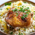 Smothered chicken and rice one pot - the image shows a plate of food with a serving of chicken and rice. the chicken is cooked to a golden brown color and appears to be seasoned with herbs and spices. the rice is white and fluffy, and there are chunks of yellow bell peppers scattered throughout the dish. the dish is garnished with a sprig of fresh parsley. the plate is made of wood and is sitting on a white marble countertop.