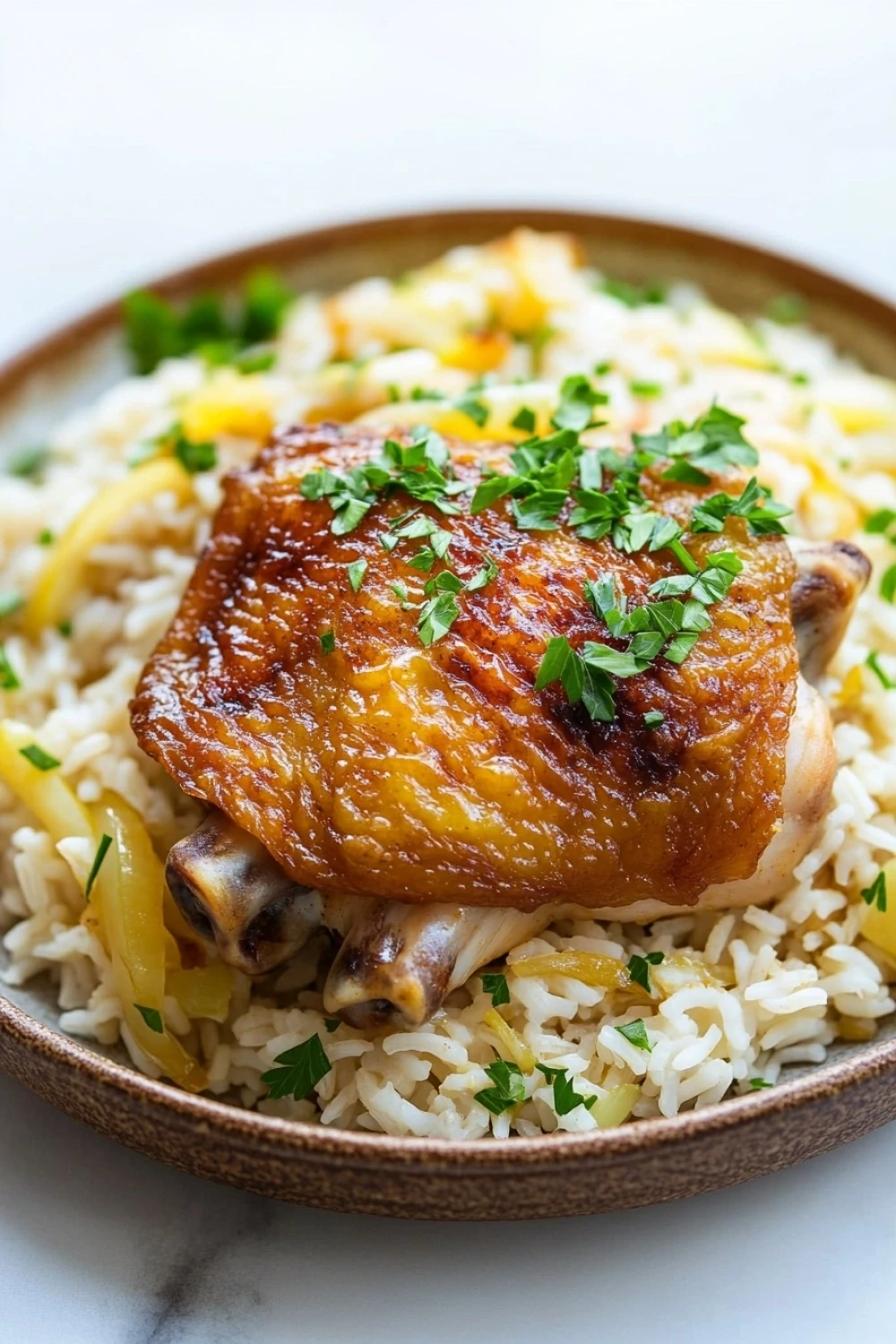Smothered chicken and rice one pot - the image shows a plate of food with a serving of chicken and rice. the chicken is cooked to a golden brown color and appears to be seasoned with herbs and spices. the rice is white and fluffy, and there are chunks of yellow bell peppers scattered throughout the dish. the dish is garnished with a sprig of fresh parsley. the plate is made of wood and is sitting on a white marble countertop.
