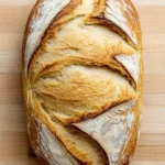 Sourdough discard sandwich bread gluten free - the image is a close-up of a freshly baked loaf of bread on a wooden cutting board. the bread appears to be golden brown in color and has a criss-cross pattern on the top and sides. the crust is slightly uneven and the inside of the bread is soft and fluffy. the loaf is resting on the cutting board with a smooth surface. the background is blurred, making the bread the focal point of the image.