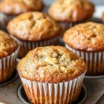 Banana muffin pictures - the image shows a group of freshly baked muffins in a muffin tin. the muffins are golden brown in color and have a crumbly texture. they are arranged in a single layer on the tray, with some overlapping each other. the tray is placed on a wooden surface, and the background is blurred, making the muffins the focal point of the image.
