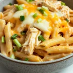 Buffalo chicken pasta freezer - the image is a close-up of a bowl of pasta dish. the pasta appears to be penne, which is a type of penne pasta, and is covered in a creamy orange sauce with chunks of chicken and melted cheese on top. the sauce is drizzled over the top of the pasta, creating a smooth and creamy texture. there are also some chopped green onions scattered throughout the dish, adding a pop of color. the bowl is made of ceramic and is sitting on a white marble countertop.