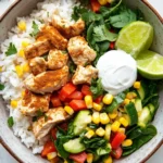Make ahead chicken rice bowls - the image is a close-up of a bowl of food. the bowl is made of ceramic and is placed on a white marble countertop. the food in the bowl appears to be a salad with rice, chicken, corn, and vegetables. the chicken is cooked to a golden brown color and is garnished with fresh cilantro and lime wedges. there is also a dollop of sour cream on top of the salad. the salad is made up of sliced cucumbers, red bell peppers, and yellow corn kernels. the overall color scheme of the dish is vibrant and colorful.