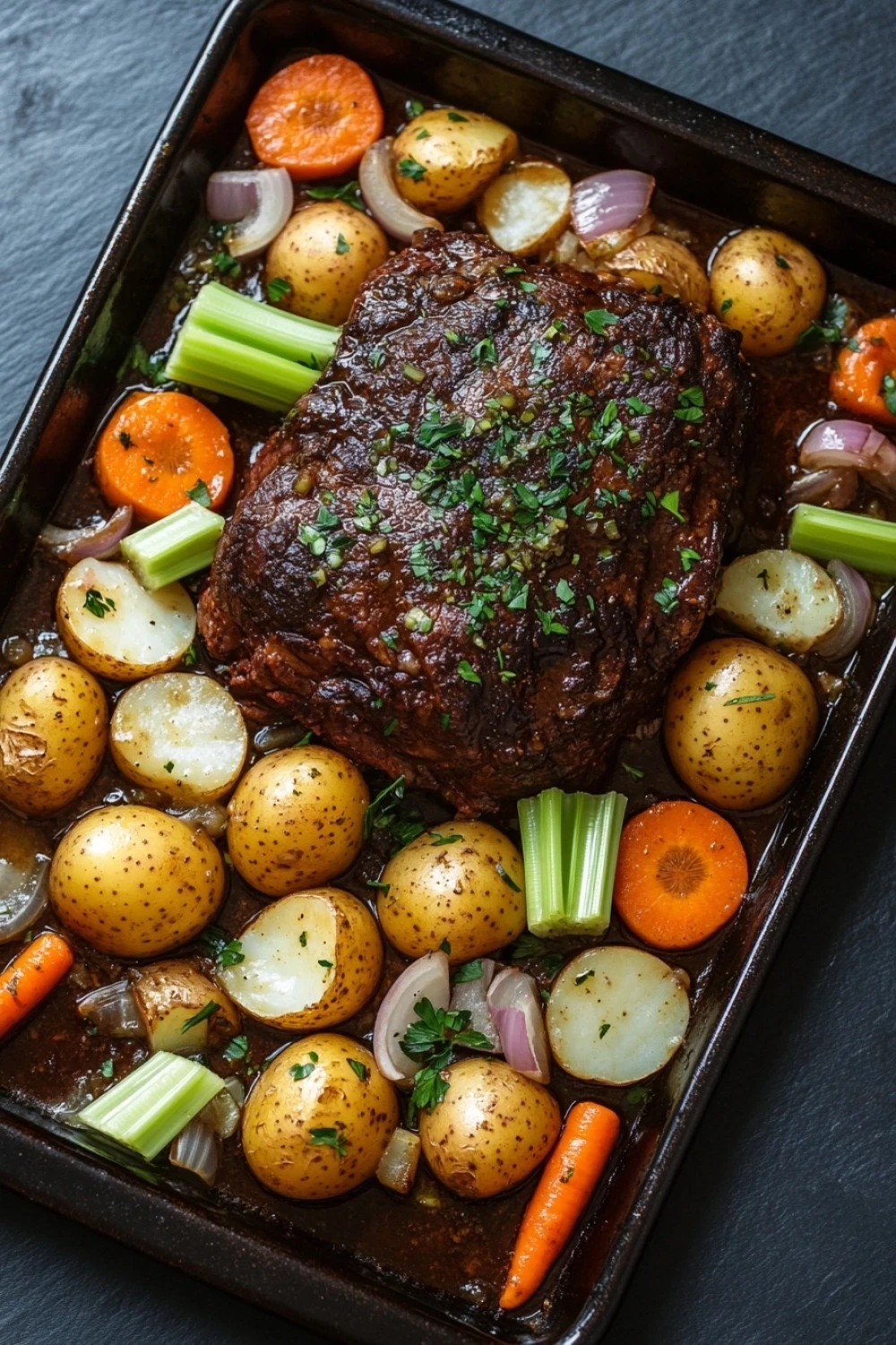 One pot pilze sahne pasta - the image shows a rectangular baking tray filled with a dish of cooked meat and vegetables. the meat appears to be a medium-rare ribeye steak, with a dark brown crust on top. it is garnished with fresh herbs and is surrounded by diced carrots, celery, onions, and potatoes. the potatoes are golden brown and appear to be seasoned with herbs and spices. the carrots are bright orange and look ripe and juicy. the celery is a vibrant green color and is scattered throughout the dish. the tray is sitting on a dark grey countertop.