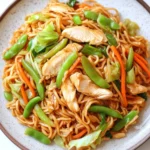 Slow cooker pot roast with potatoes - the image is a close-up of a plate of noodles with chicken and vegetables. the noodles are light brown in color and appear to be stir-fried. the dish is garnished with sliced carrots, snow peas, and green onions. the chicken is cut into small pieces and is scattered throughout the dish. the vegetables are bright green and look fresh and vibrant. the plate is white with a brown rim and is sitting on a white marble countertop.