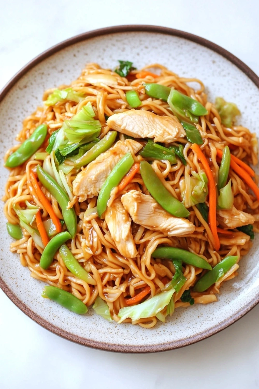Slow cooker pot roast with potatoes - the image is a close-up of a plate of noodles with chicken and vegetables. the noodles are light brown in color and appear to be stir-fried. the dish is garnished with sliced carrots, snow peas, and green onions. the chicken is cut into small pieces and is scattered throughout the dish. the vegetables are bright green and look fresh and vibrant. the plate is white with a brown rim and is sitting on a white marble countertop.