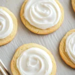 Sugar cookie and royal icing - the image shows a baking tray lined with freshly baked cookies. the cookies are round and golden brown in color, and they are arranged in a single layer on the tray. each cookie has a swirl of white frosting on top, creating a swirl-like pattern. the frosting appears to be smooth and creamy, and the cookies look soft and fluffy. the tray is lined with parchment paper, and there is a wooden table in the background.