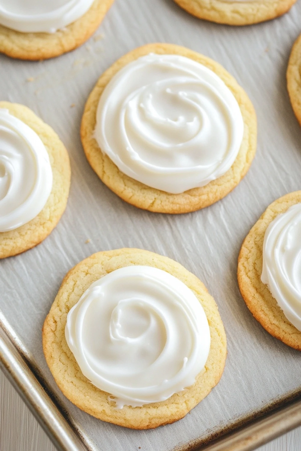 Sugar cookie and royal icing - the image shows a baking tray lined with freshly baked cookies. the cookies are round and golden brown in color, and they are arranged in a single layer on the tray. each cookie has a swirl of white frosting on top, creating a swirl-like pattern. the frosting appears to be smooth and creamy, and the cookies look soft and fluffy. the tray is lined with parchment paper, and there is a wooden table in the background.