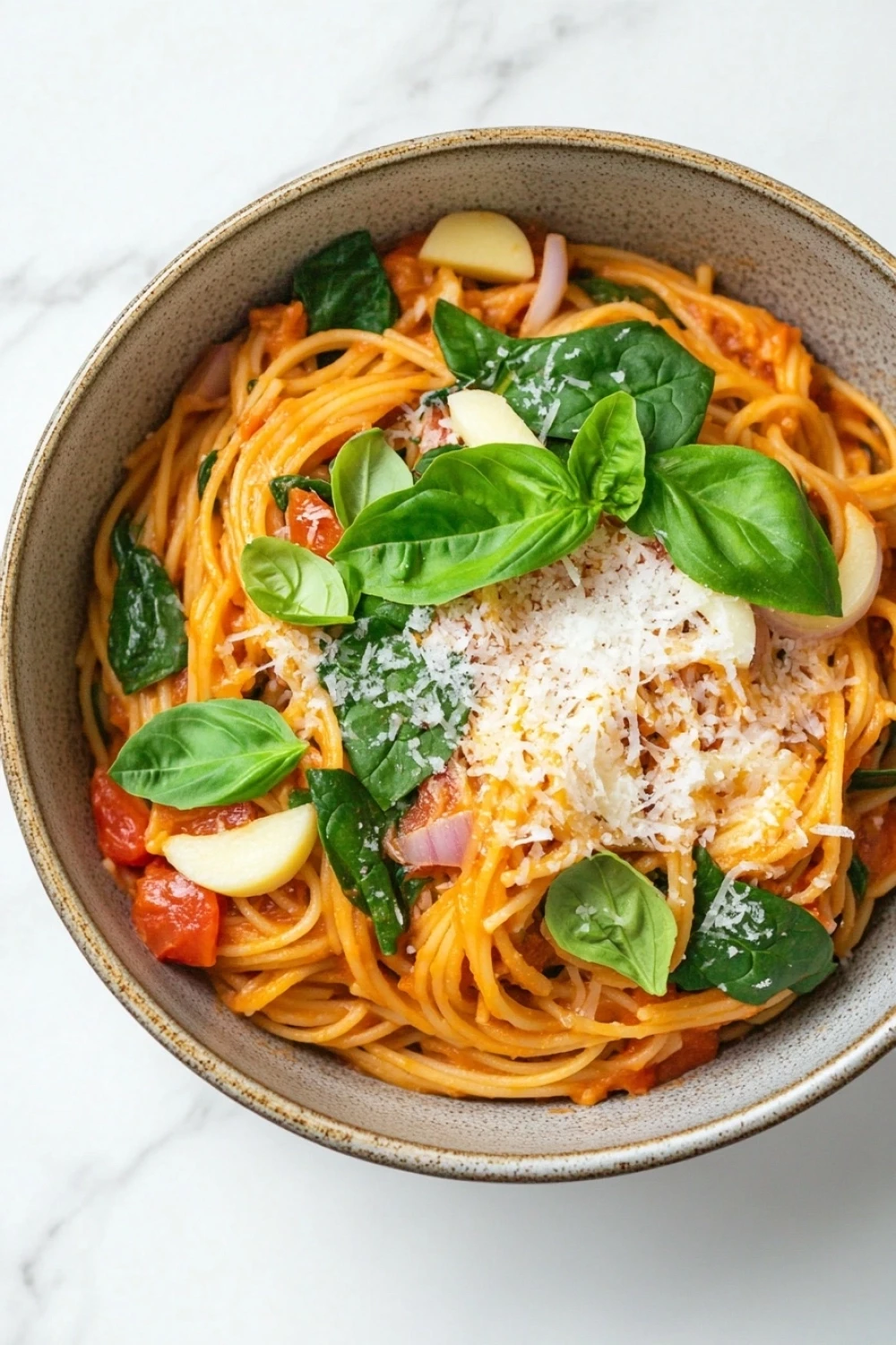 Ultimate one pot pasta - the image is a close-up of a bowl of spaghetti dish. the spaghetti is cooked al dente and is topped with tomato sauce, sliced tomatoes, and fresh basil leaves. the dish is garnished with grated parmesan cheese. the bowl is made of ceramic and is sitting on a white marble countertop. the overall color scheme of the dish is warm and inviting.